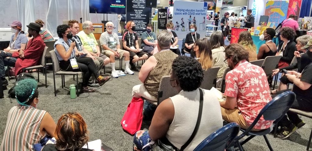 eight people sitting in a semicircle in front of multiple people seated while listening to the speaker